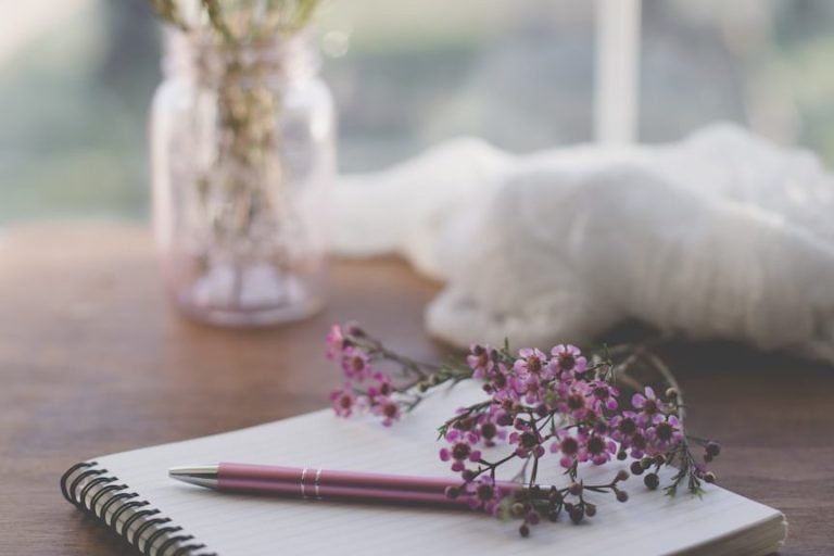 Eine Kerze, Notizbuch, Brille und Pflanzen auf einem Tisch.